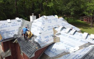 Roofers working on a residential roof installation with shingles and underlayment.