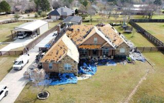 Roofers working on a house with damaged shingles and roofing materials.