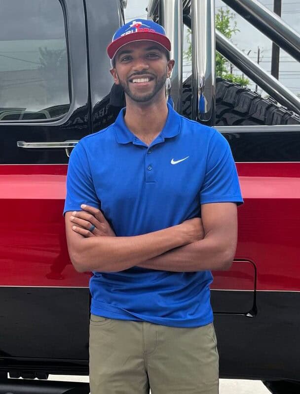 Roofing professional in blue polo shirt standing in front of a truck.