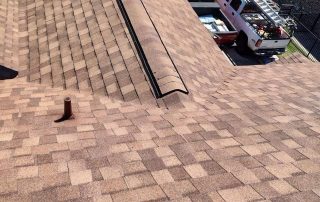 Roofers working on a sloped roof with multiple layers of shingles.